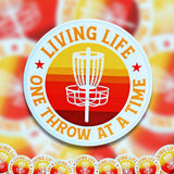 A pile of Livin' Life One Throw at a Time disc golf stickers. 