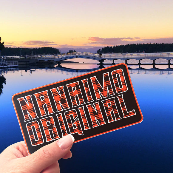 A hand holding a Nanaimo Original sticker at Swy-a-lana Lagoon in Nanaimo.