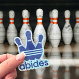 An Abides sticker in front of a bunch of bowling pins. 