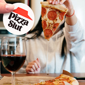 A person holding a piece of pizza in front of a Pizza Slut sticker.