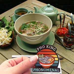 A Pho-King Phonomenal sticker in front of a table full of pho. 